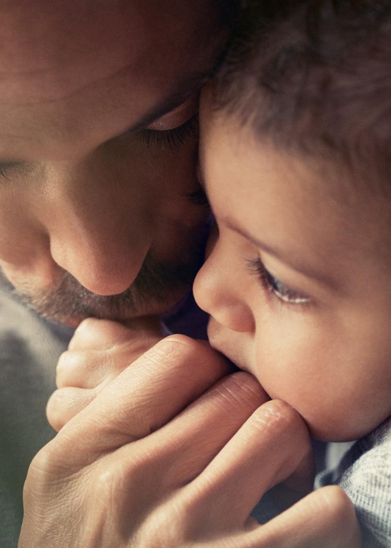 A close-up of a father tenderly embracing his baby, both resting their heads together, conveying warmth and affection.